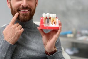 man holding up a dental implant model, pointing to his mouth 