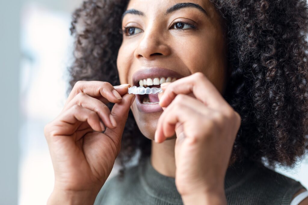 closeup of a woman putting in her Invisalign, clear aligner therapy for a straighter smile
