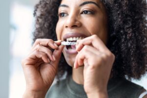 closeup of a woman putting in her Invisalign, clear aligner therapy for a straigter smile